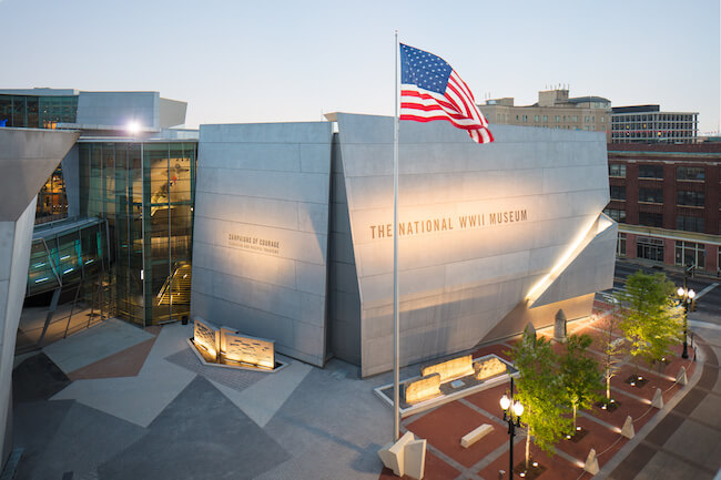 An exterior shot of The National WWII Museum in New Orleans, LA at dusk, with an American flag waving out front.