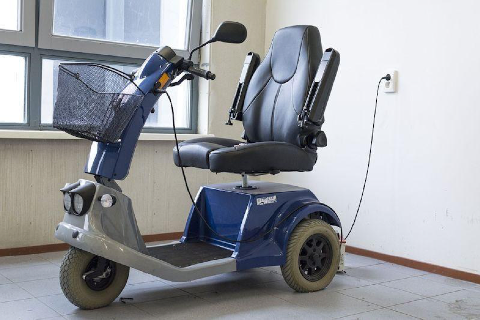 A photo of a mobility scooter plugged in and getting recharged in a well-lit apartment.