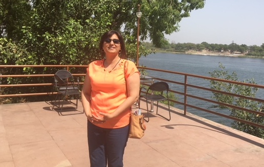Project Starfish lead Nasreen Bhutta stands on a deck overlooking a lake, wearing sunglasses, black pants and an orange top.