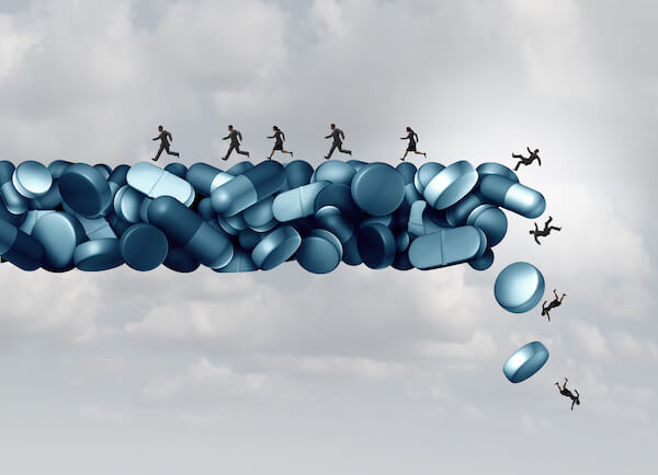 A graphic illustration of small silhouettes of people running and tumbling off of a cliff made of blue pills, with a gray, cloudy sky as a backdrop.