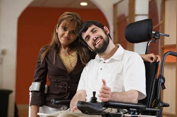 A man in a motorized wheelchair and a woman with a forearm crutch pose together, smiling.