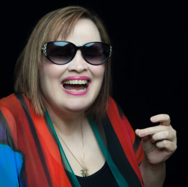Jazz artist Diane Schuur smiles, wearing sunglasses and snapping her fingers.